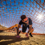 Participant crawling under the net while smiling in the heat of the sun