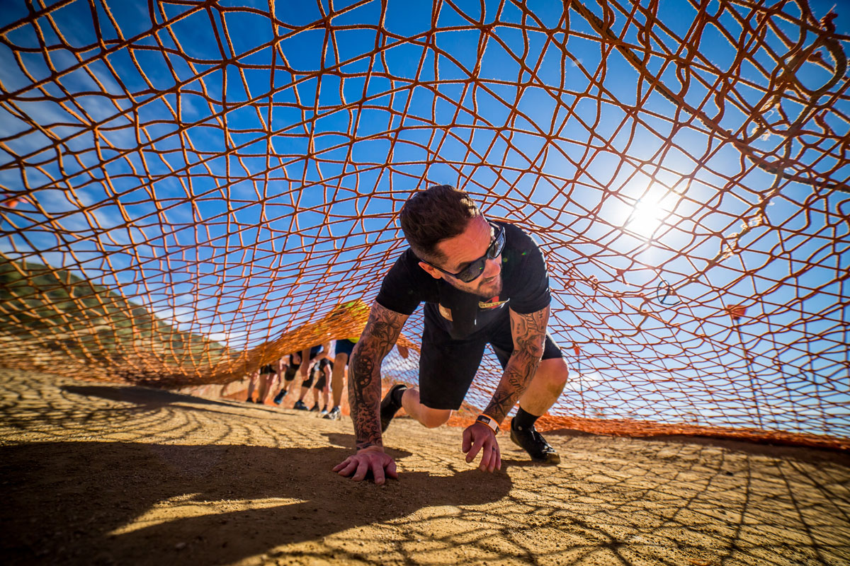 Participant crawling under the net while smiling in the heat of the sun