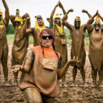 Participants in banana outfit standing behind a kneeling participant wearing orange outfit